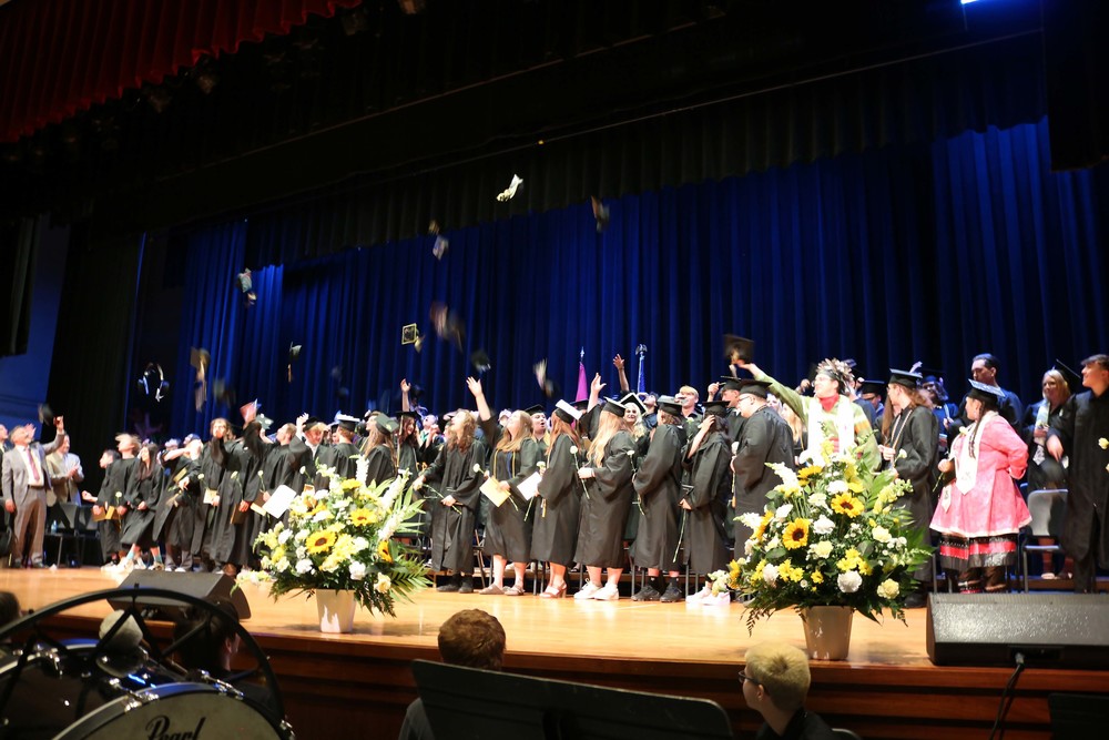 The Class of 2023 members toss their graduation caps in the air while on stage in the auditorium.