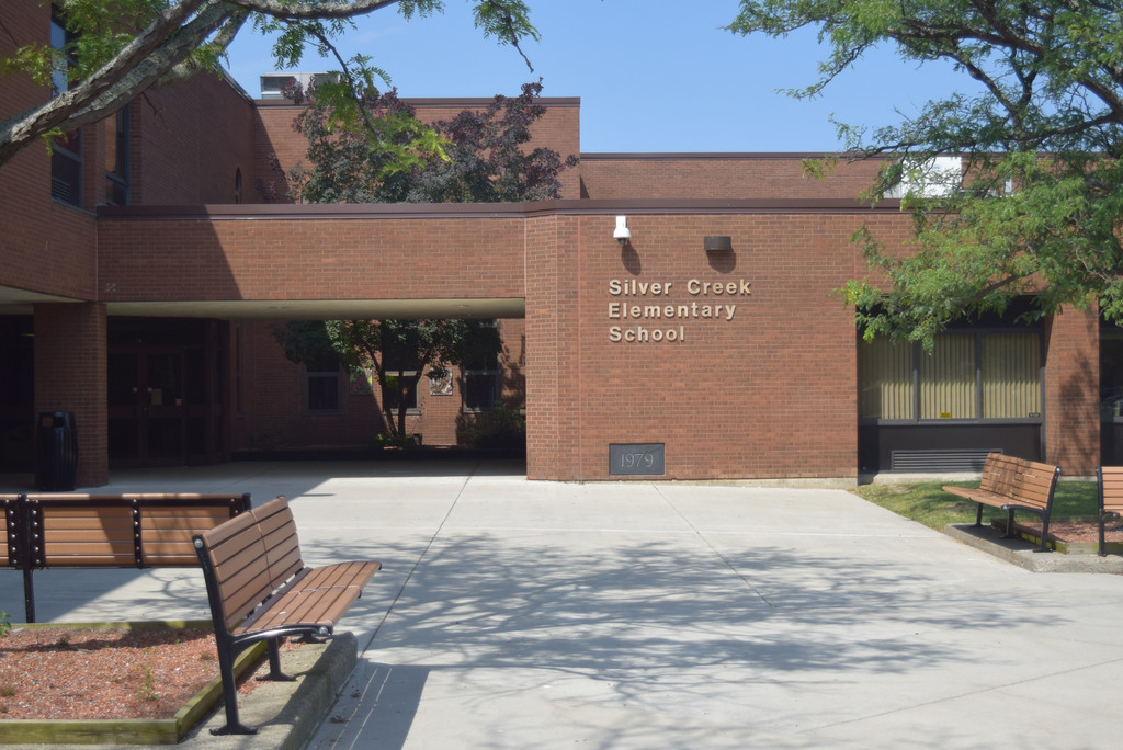 The exterior and main entrance of Silver Creek Elementary School. Brick building with benches in front and trees to the side.