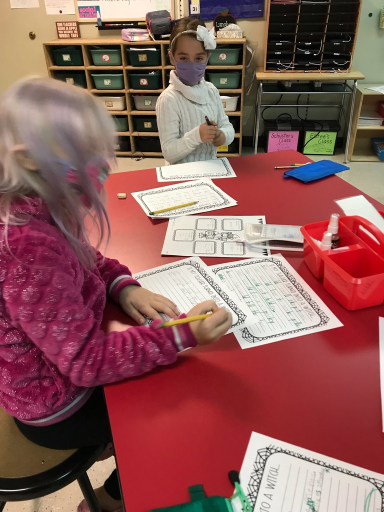 Two students wearing masks work on their witch writing assignment