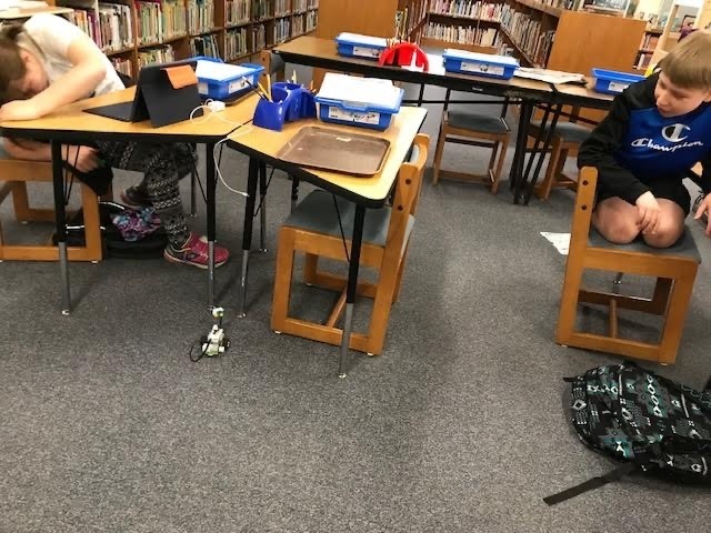 student sitting it desks in the library work together on coding and robots