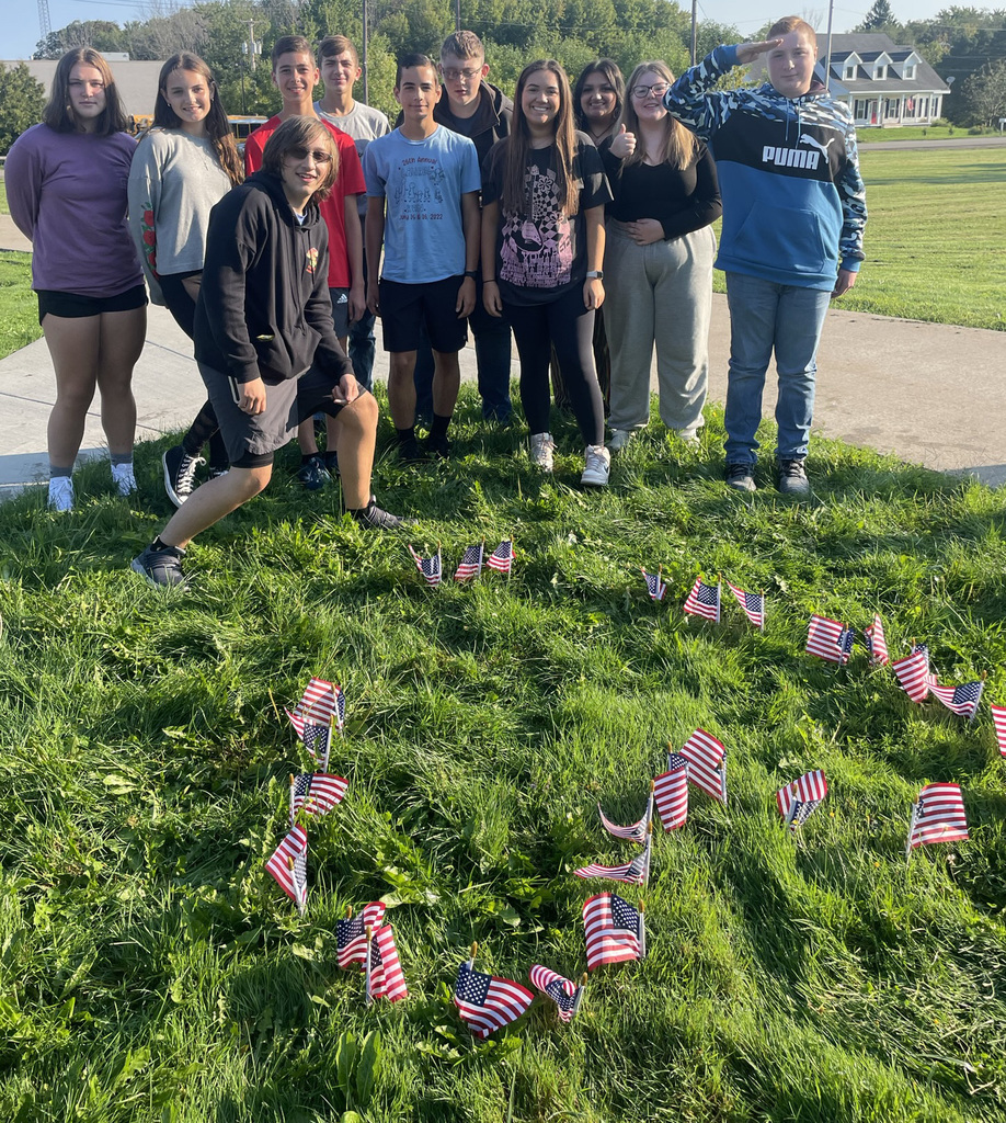 students smile behind their lawn heart made out of flags 